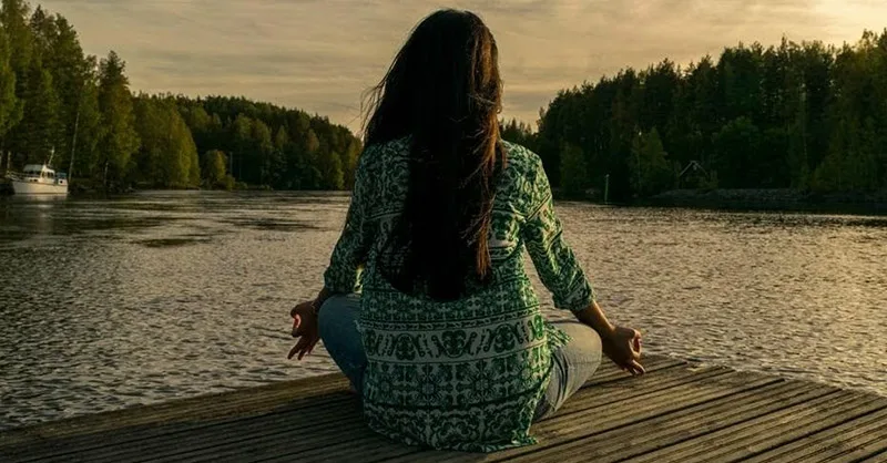 Bien-être mental : une personne, une femme méditant au bord de la rivière.