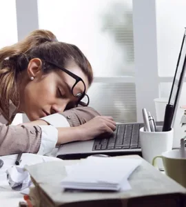 Burn-out : image d'une personne, une femme, un employé fatiguée la tête posée sur le bureau, des dossiers empilés.