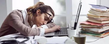 Burn-out : image d'une personne, une femme, un employé fatiguée la tête posée sur le bureau, des dossiers empilés.