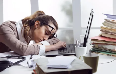 Burn-out : image d'une personne, une femme, un employé fatiguée la tête posée sur le bureau, des dossiers empilés.