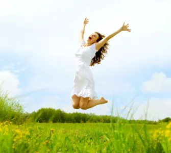 Alimentation anti-fatigue : image, photo d'une personne, une femme pleine d’énergie, en train de sauter dans un champ ensoleillé ou de sourire avec les bras ouverts.