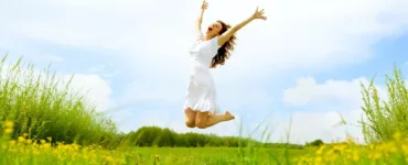 Alimentation anti-fatigue : image, photo d'une personne, une femme pleine d’énergie, en train de sauter dans un champ ensoleillé ou de sourire avec les bras ouverts.