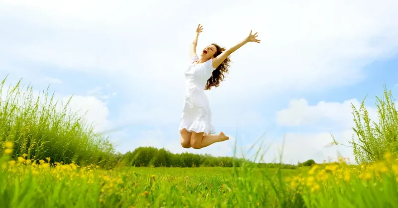 Alimentation anti-fatigue : image, photo d'une personne, une femme pleine d’énergie, en train de sauter dans un champ ensoleillé ou de sourire avec les bras ouverts.