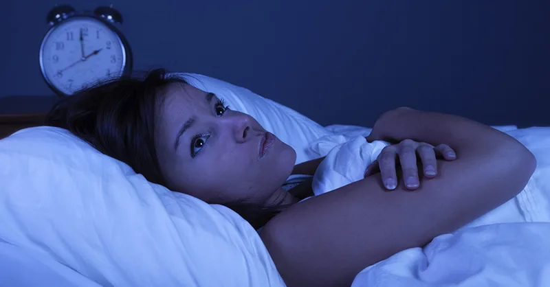 Insomnie : image d'une personne, une femme allongée dans son lit, les yeux grands ouverts, regardant le plafond.