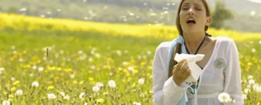 Les allergies : image, photo d'une personne, une femme éternuant dans un champ de fleurs au printemps.